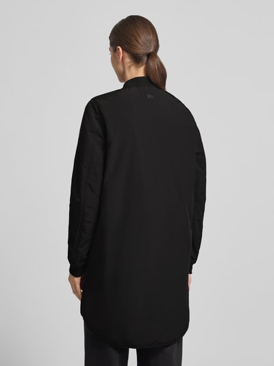 Modelka nosi czarną Kurtkę 'Jacke mit Zweiwege-Reißverschluss' od camel active o luźnym kroju, stójka, elastyczne zakończenia rękawów, bardzo długi krój, długość tyłu w rozmiarze 36: 92 cm, szerokość ramion: 42 cm, szerokość w rozmiarze 36: 55 cm, długość rękawów: 64 cm. Ganzkörperansicht Rückansicht.