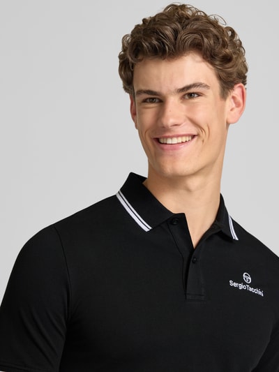 Männermodel trägt schwarzes Slim Fit Poloshirt mit Logo-Stitching Modell 'Reed' von SERGIO TACCHINI aus Baumwoll-Mix, Nahaufnahme Oberkörper.