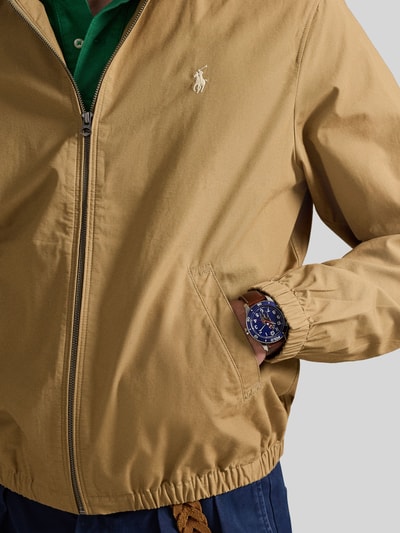 Mannenmodel draagt Regular Fit blouson uit puur katoen van Polo Ralph Lauren, look: effen, logodetail, steekzakken, ritssluiting, lange mouw, platte kraag, elastische rompzoom en mouwboord, kleur beige, detailopname bovenlichaam.