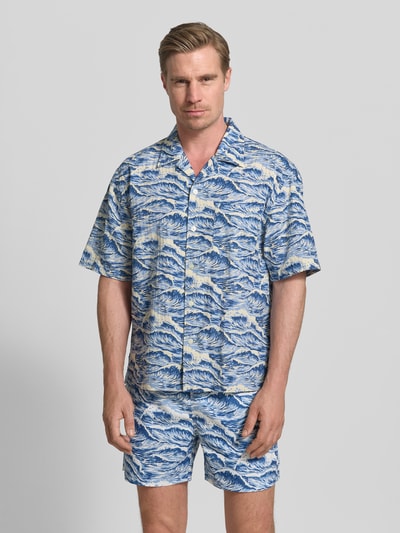 Męski model nosi Relaxed Fit Freizeithemd mit Reverskragen von Gant z bawełny, krój relaxed fit, kołnierz z połami, listwa guzikowa, z krótkim rękawem, brustasza, długość tyłu w rozmiarze M: 71 cm, szerokość w rozmiarze M: 57 cm, długość rękawów w rozmiarze M: 29 cm, wzór niebieski, tekstura gładka, całkowity widok z przodu.