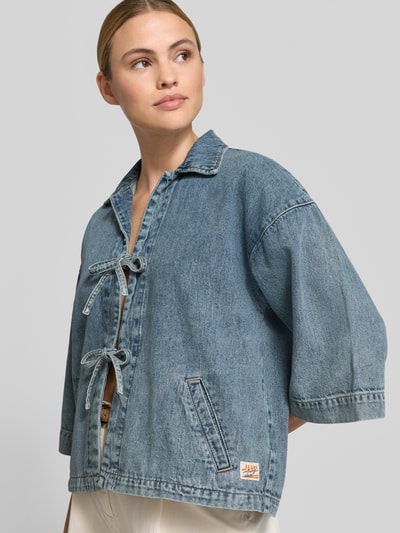 Frauenmodel trägt Jeansjacke mit Kimonoärmel Modell 'ZOE' von Mustang, Reine Baumwolle, Regular-Fit, Umlegekragen, Schnürverschluss, seitliche Eingrifftaschen, mittleres Blau, glatte Textur, Rückenlänge bei Größe S 56 cm, Schulterbreite 44 cm, Brustweite 54 cm, Ärmellänge 43 cm, Ganzkörperansicht von vorne.