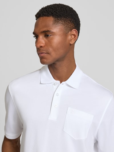 Männermodel trägt Regular Fit Poloshirt mit Brusttasche und Label-Stitching von bugatti in Weiß, glatte Textur, Nahaufnahme Oberkörper. Herren Poloshirt mit Polokragen, Knopfleiste, Rückenlänge 70 cm bei Größe M.