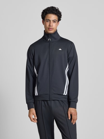 Männermodel trägt Sweatjacke mit Reißverschlusstaschen Modell 'TOSCIANA' von Ellesse, Schwarz, Material-Mix mit Stretch-Anteil, Ganzkörperansicht von vorne.