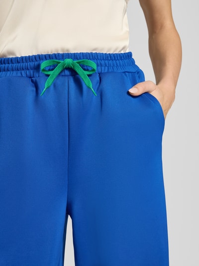 Frauenmodel trägt Sweatpants mit weitem Bein und elastischem Bund Modell 'Liam' von Lollys Laundry, Material-Mix mit Stretch-Anteil, Tunnelzug mit grünem Band, Farbe Blau, Nahaufnahme Oberkörper.