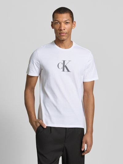 Männermodel trägt T-Shirt mit Rundhalsausschnitt und Logo von CK Calvin Klein aus reiner Baumwolle, Regular-Fit, weiß, Logo-Print, Nahaufnahme Oberkörper. Rückenlänge bei Größe M: 70 cm.