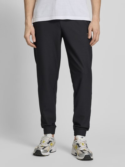 Mężczyznamodel nosi Regular Fit Sweatpants mit Strukturmuster od EA7 Emporio Armani, czarne z fakturą, elastyczny pas, kieszenie, widok z przodu, detal nogawek, krój regular fit, długość nogawki wewnętrznej w rozmiarze M: 79 cm.