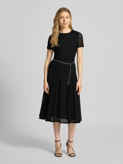 Frauenmodel trägt Midikleid mit Gürtel in Gliederketten-Optik von MICHAEL Michael Kors, schwarzer Material-Mix mit Stretch-Anteil, taillierter Schnitt, Rundhalsausschnitt, blickdichtes Unterkleid, Rückseitiger Schlüsselloch-Ausschnitt, Rückenlänge bei Größe S: 116 cm, Brustweite bei Größe S: 40 cm, Ärmellänge bei Größe S: 20 cm, Ganzkörperansicht von vorne.