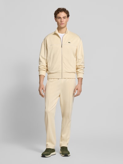 Männermodel trägt Regular Fit Sweatpants mit Baumwoll-Anteil von Lacoste in Creme, unifarben, mit Logo und Galonstreifen, Ganzkörperansicht von vorne.