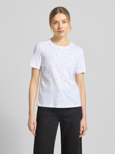 Modelka kobieca nosi Shaped Fit T-Shirt aus reiner Baumwolle Modell 'PAULINA AOP' od Vero Moda, biały kolor, wzór allover, okrągły dekolt, krótki rękaw, jersey, widok całej sylwetki z przodu.