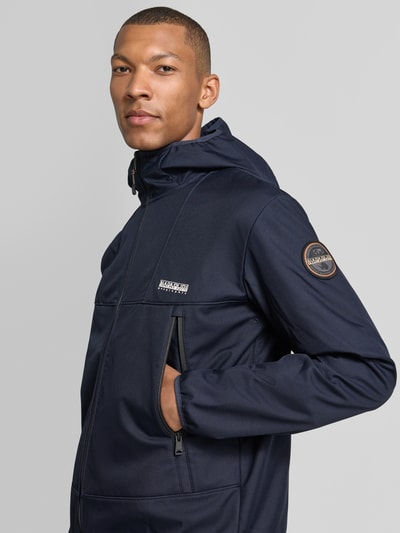 Męski model nosi Regular Fit Jacke mit Logo-Print von Napapijri w kolorze granatowym, stójka, wpuszczane kieszenie z zamkiem błyskawicznym, elastyczne wykończenia, nadruk z logo, krój regular fit, długość tyłu w rozmiarze M: 69 cm, szerokość ramion w rozmiarze M: 52 cm, szerokość klatki piersiowej w rozmiarze M: 60 cm, długość rękawów w rozmiarze M: 68 cm, zbliżenie na górną część ciała z przodu.