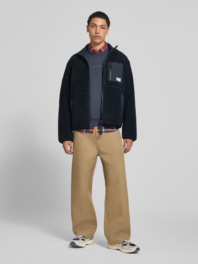 Männermodel trägt schwarze Regular Fit Teddy- / Webpelzjacke mit Brustleistentaschen von Marc O'Polo, kombiniert mit beigen Hosen; Ganzkörperansicht von vorne. Herren Teddy- / Webpelzjacke von Marc O'Polo DENIM.