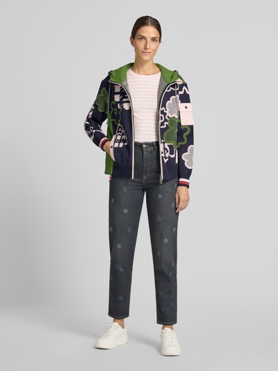 Frauenmodel trägt Regular Fit Jacke mit floralem Allover-Stitching von Marc Cain, bunte Farben, Kapuze mit Tunnelzug, Ganzkörperansicht von vorne.