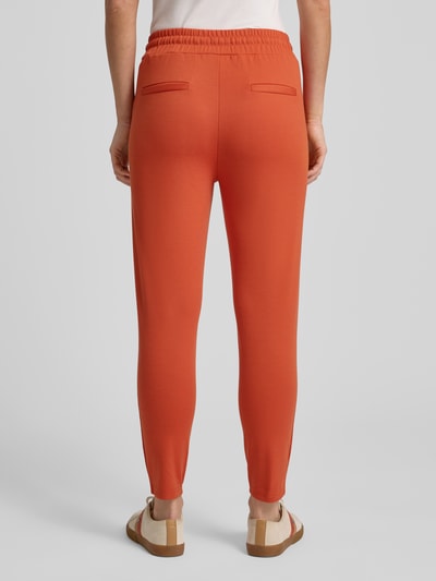 Frauenmodel trägt Stoffhose mit elastischem Bund Modell 'KATE' von ICHI in Orange, Material-Mix mit Viskose-Anteil, Gerader-Schnitt, Gesäßtaschen, Ganzkörperansicht Rückansicht.