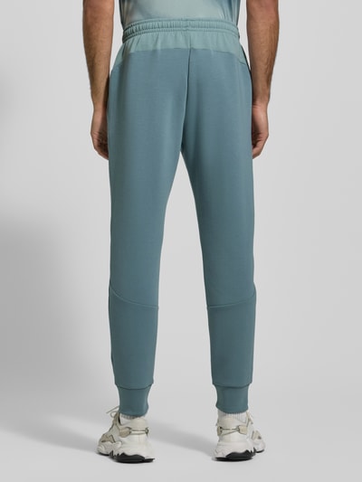 Męski model nosi Sweatpants mit Logo Modell 'Unstoppable' od Under Armour, kolor niebiesko-szary, regular fit, widok całej sylwetki z tyłu.