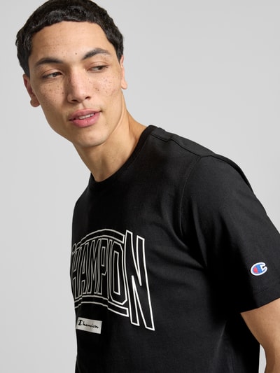 Männermodel trägt T-Shirt mit Logo und Rundhalsausschnitt von CHAMPION in Schwarz, reine Baumwolle, Regular Fit, Nahaufnahme Oberkörper.