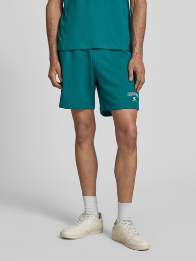 Männermodel trägt Sweatshorts mit Logo und elastischem Bund von CHAMPION in Türkis, Regular Fit, Baumwoll-Mix, Nahaufnahme Oberkörper bis Knie.