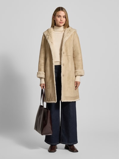 Modelka kobieca nosi Wendemantel mit Kapuze und Eingrifftaschen od PETITE M., beżowy kolor, sztuczne futro, regular fit, widok całej sylwetki z przodu.