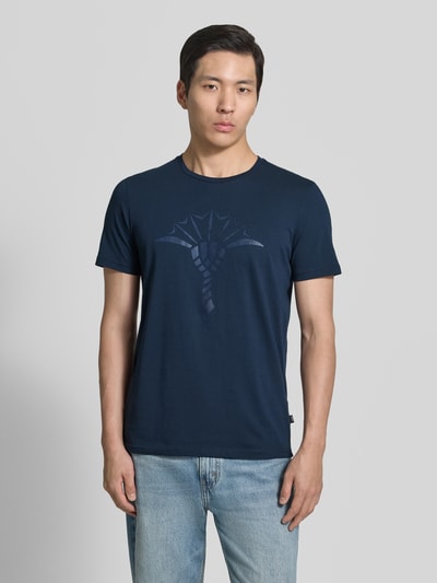 Männermodel trägt Herren T-Shirt mit Rundhalsausschnitt Modell 'Alerio' von JOOP! Collection, Reine Baumwolle, Regular-Fit, Logo, Dunkelblau, glatte Struktur, Ganzkörperansicht von vorne.