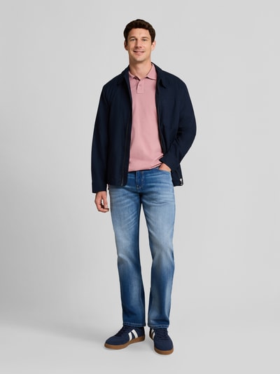 Männermodel trägt Regular Fit Poloshirt aus Baumwoll-Mix von Tom Tailor in Rosa, kombiniert mit blauer Jeans, Ganzkörperansicht von vorne. Herren Poloshirt von Tom Tailor
