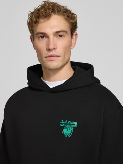 Männermodel trägt Relaxed Fit Hoodie mit Motiv-Print von REVIEW x ANSON´S, schwarzer Baumwoll-Mix, Nahaufnahme Oberkörper.