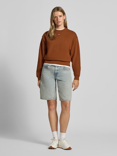 Frauenmodel trägt Regular Fit Sweatshirt aus reiner Baumwolle Modell 'Delessa_B' von HUGO in Braun, kombiniert mit Jeansshorts, Damen Sweatshirt von HUGO Blue, Ganzkörperansicht von vorne.