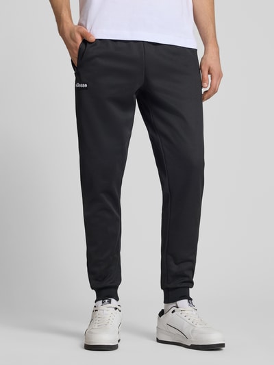Męskamodel nosi spodnie dresowe Sweatpants mit elastischem Bund Modell 'BERTONI' od Ellesse, mieszanka bawełny, krój regular fit, z detalem z logo, długość wewnętrzna nogawki w rozmiarze M: 76 cm; całkowita sylwetka z przodu.