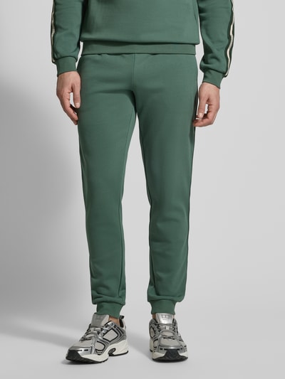 Männermodel trägt grüne Sweatpants aus Baumwoll-Mix von EA7 Emporio Armani mit elastischem Bund, Tunnelzug, Eingrifftaschen, lockerer Passform, elastischen Beinabschlüssen und 78 cm Innenbeinlänge bei Größe M, Nahaufnahme Unterkörper.