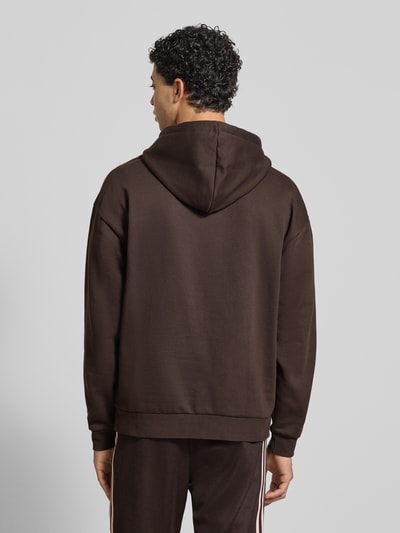 Männermodel trägt Oversized Hoodie mit Kapuze von adidas Originals in Dunkelbraun, Baumwoll-Mix, Känguru-Tasche, Rückenansicht Ganzkörperansicht.