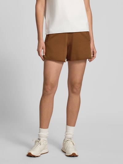 Frauenmodel trägt Sweatshorts mit Eingrifftaschen von Rich & Royal aus Baumwoll-Mix mit Stretch-Anteil, Relaxed-Fit, elastischer Bund, Tunnelzug, Innenbeinlänge bei Größe S 14 cm, braune Farbe, glatte Struktur. Ganzkörperansicht von vorne.