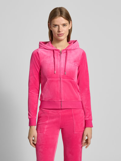 Frauenmodel trägt Sweatjacke mit Label-Stitching Modell 'ROBERTSON' von Juicy Couture in Pink, Material-Mix mit Stretch-Anteil, Regular-Fit, Kapuze mit Tunnelzug, Reißverschluss und Känguru-Tasche, Ganzkörperansicht von vorne.