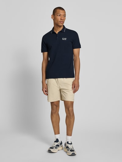 Mężczyzn-model nosi Regular Fit Poloshirt mit Logo-Print od EA7 Emporio Armani, granatowy, bawełniany, z krótkim rękawem, widok całej sylwetki z przodu.