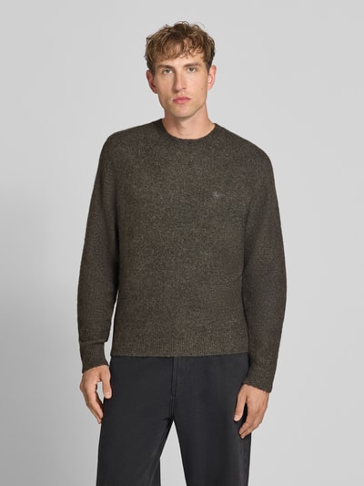 Männermodel trägt dunkelbraunen Strickpullover mit Logo-Stitching Modell 'CURTIS' von Carhartt Work In Progress, lockerer Schnitt, Material-Mix, Rundhalsausschnitt, gerippte Abschlüsse, Ganzkörperansicht von vorne.