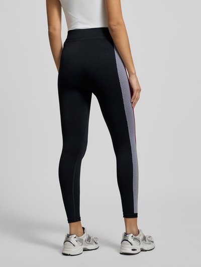 Frauenmodel trägt Leggings mit Galonstreifen Modell 'SEAMLESS' von Tommy Hilfiger, eng anliegend, schwarz mit seitlichem Streifen, elastischer Bund, Material-Mix mit Stretch, Ganzkörperansicht Rückansicht.