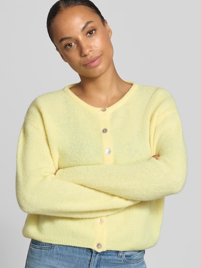 Frauenmodel trägt Relaxed Fit Strickjacke aus Woll-Mix mit Leinen-Anteil von American Vintage in Hellgelb, melierte Textur, gerippte Bündchen, durchgehende Knopfleiste, Damen Strickjacke, Nahaufnahme Oberkörper.