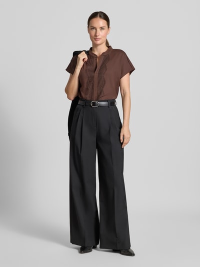 Frauenmodel trägt Regular Fit Bluse aus Baumwoll-Mix mit Spitzenbesatz von Marc Cain in Braun, kombiniert mit weiter schwarzer Hose, Ganzkörperansicht von vorne. Damen Bluse, elastischer Baumwoll-Mix, Serafino-Ausschnitt, Kurzarm, Rückenlänge bei Größe 36: 57 cm.