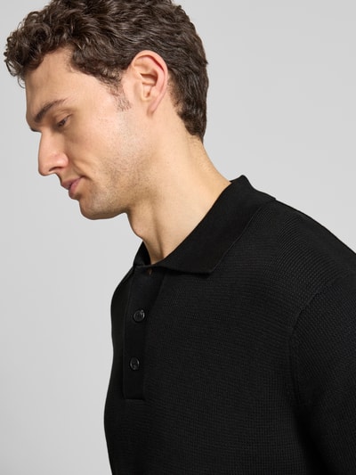 Männermodel trägt Relaxed Fit Poloshirt aus reiner Baumwolle Modell 'DANE' von SELECTED HOMME in Schwarz, Strickoptik, Nahaufnahme Oberkörper.