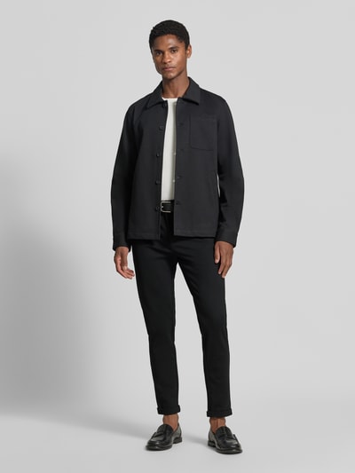Mannelijk model draagt Slim Fit Stoffhose met omgeslagen broekspijpen van Lindbergh, elastische materiaalmix met viscose, slim fit, riemlussen, knoop- en ritssluiting, bandwijdte maat M 43 cm, binnenbeenlengte maat M 73 cm, zwarte kleur, gladde textuur, geheel lichaamsaanzicht van voren.
