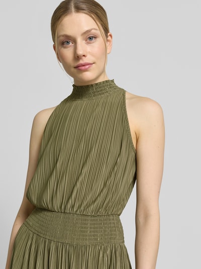 Frauenmodel trägt Plisseekleid mit Smok-Details Modell 'UMA' von Samsøe Samsøe in Oliv, Material-Mix mit Stehkragen, Nahaufnahme Oberkörper.