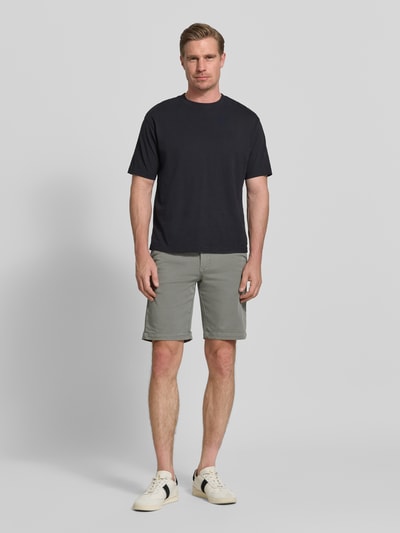 Männermodel trägt Bermudas mit Bindegürtel und französischen Eingrifftaschen von MAC in hellem Grau, Baumwoll-Mix mit Stretch-Anteil, Straight Fit, Knopf- und Reißverschluss, Gesäßleistentaschen mit Knopfverschluss, rückseitiger Label-Print, Bundweite bei Größe 32: 42 cm, Innenbeinlänge bei Größe 32: 26 cm; Ganzkörperansicht von vorne.