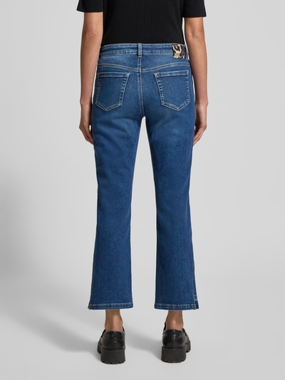 Vrouwenmodel draagt Feminine Fit Jeans in verkorte pasvorm van Marc Cain, blauwe katoen-elastaan mix met steekzakken, volledige achteraanzicht.