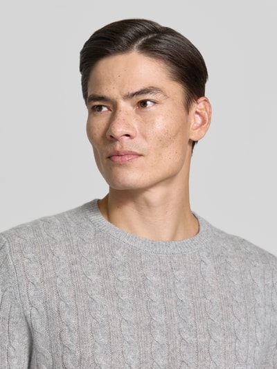 Mężczyzna nosi Slim Fit Strickpullover aus reinem Kaschmir mit Zopfmuster od Christian Berg Men, jasnoszary kolor, ścieg warkoczowy, prążkowane wykończenia, okrągły dekolt, sweter z kaszmiru, krój slim fit, detaliczny widok górnej części ciała z przodu.
