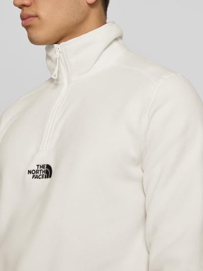 Männermodel trägt Fleecepullover mit Reißverschluss Modell 'GLACIER' von The North Face in Weiß, Label-Stitching, Nahaufnahme Oberkörper, Regular Fit, Stehkragen, Rückenlänge 70 cm, Ärmellänge 67 cm.