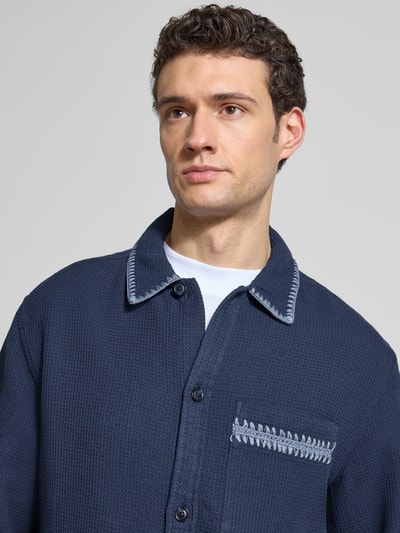 Männermodel trägt Relaxed Hemdjacke mit Strukturmuster von Scotch & Soda in Dunkelblau, reine Baumwolle, Nahaufnahme Oberkörper.