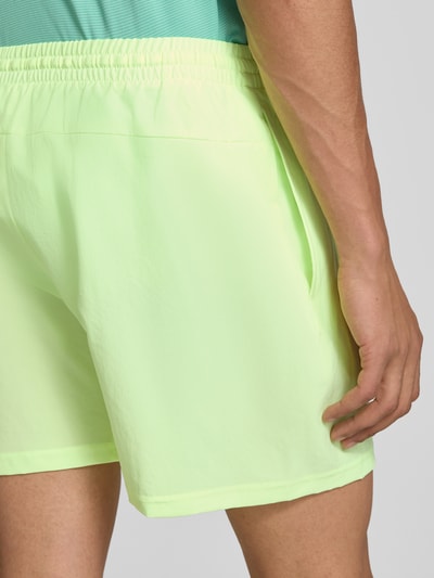 Männermodel trägt Shorts mit elastischem Bund und Logo von New Balance in Regular-Fit, neonfarben, glatte Struktur, Nahaufnahme Rückansicht.