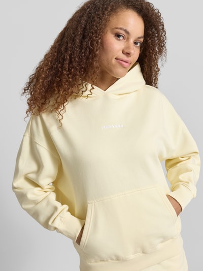 Frauenmodel trägt Oversized Hoodie mit Label-Stitching Modell 'CLARITA' von Pegador aus Baumwoll-Mix in Pastellgelb mit Känguru-Tasche, Nahaufnahme Oberkörper.