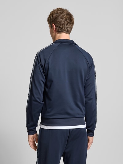 Männermodel trägt Trainingsjacke mit aufgesetztem Band auf Raglanärmeln von REVIEW in Dunkelblau, Rückenansicht, Ganzkörperansicht Rückansicht.