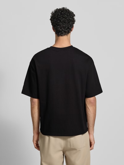 Męski model nosi Oversized Fit T-Shirt mit Logo-Stitching od REVIEW, czarny, bawełna, florystyczne przeszycia, tył, widok całej sylwetki od tyłu.