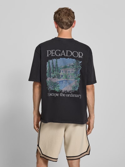 Männermodel trägt Oversized Herren T-Shirt aus Reine Baumwolle von PEGADOR, Modell 'Trofa' mit Label-Print, Rückenlänge 69 cm, Ganzkörperansicht Rückansicht.