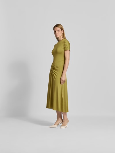 Frauenmodel trägt Midikleid mit Raffungen von Victoria Beckham in Olivgrün, taillierte Passform, Rundhalsausschnitt, Kurzarm, Ganzkörperansicht von vorne.