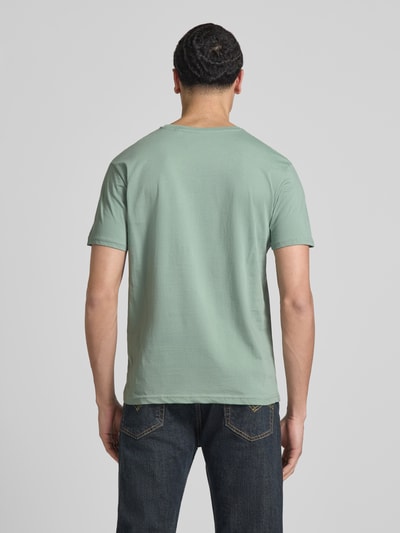 Männermodel trägt T-Shirt mit Label-Details Modell 'BASIC' von Alpha Industries in Grün, Reine Baumwolle, Gerader-Schnitt, Rückenlänge 67 cm, Ganzkörperansicht Rückansicht.